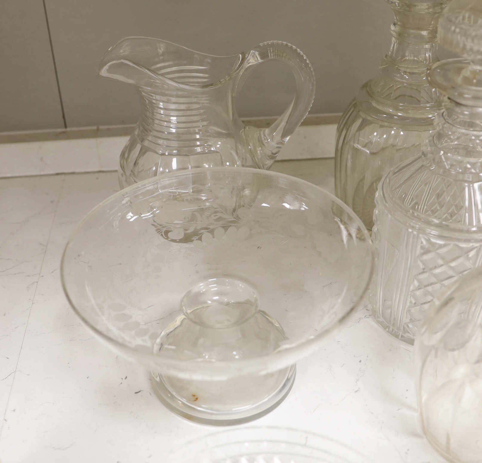 A collection of cut glass decanters and other glassware including five decanters with stoppers, three carafes, two jugs, five shallow round dishes, a pedestal dish, four Crescent dishes and a rinser, tallest 25cm